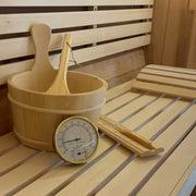 Accessoires de sauna en bois avec seau, louche, thermomètre et sablier posés sur un banc